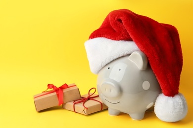 Photo of Piggy bank with Santa hat and gift boxes on yellow background. Space for text