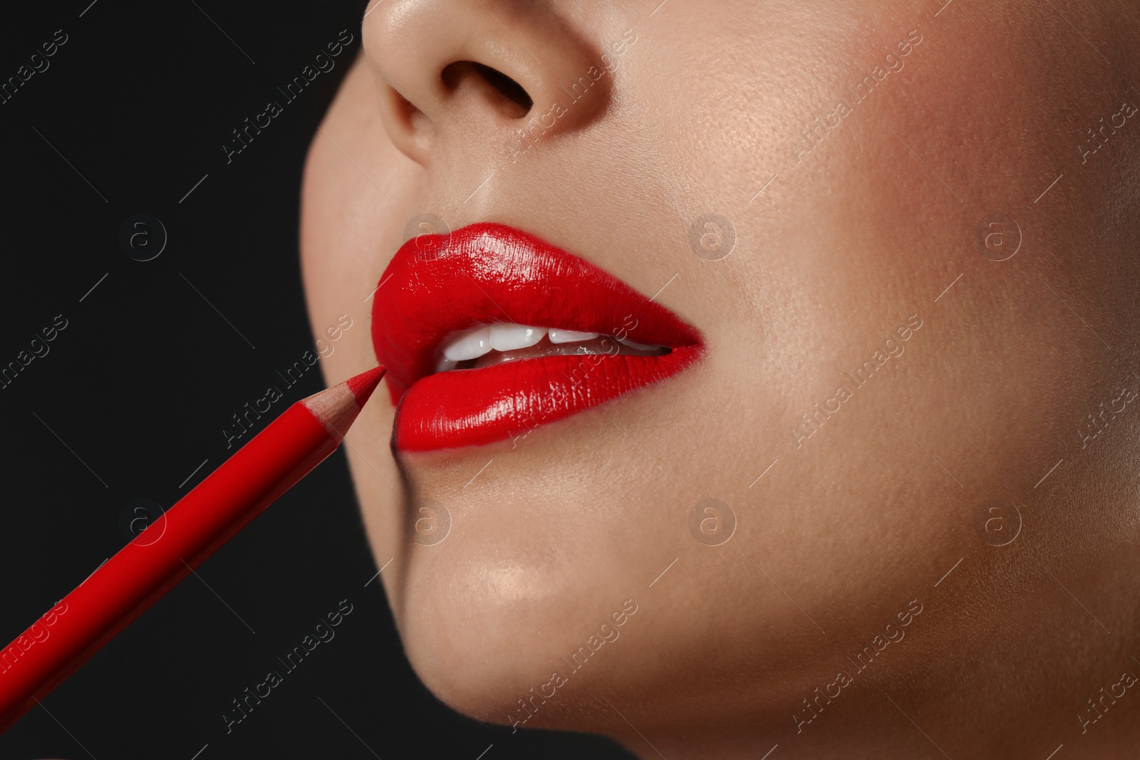 Photo of Young woman applying beautiful red lip pencil on black background, closeup