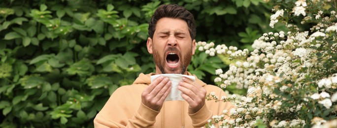 Man suffering from seasonal pollen allergy near blossoming tree on spring day. Banner design