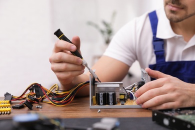 Male technician repairing power supply unit at table indoors, closeup