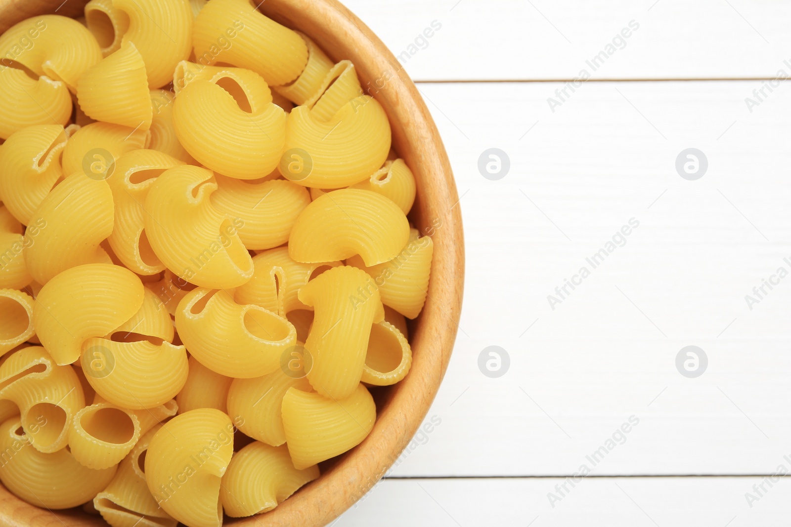 Photo of Raw macaroni pasta in bowl on white wooden table, top view. Space for text