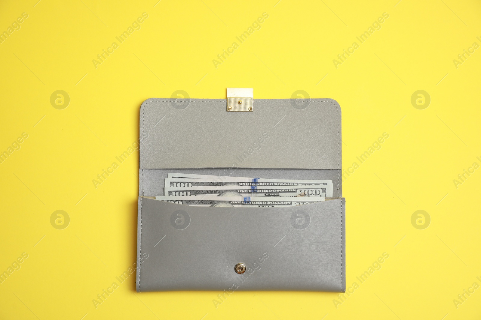 Photo of Stylish light grey leather purse with dollar banknotes on yellow background, top view