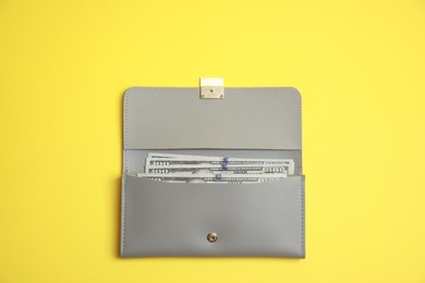 Photo of Stylish light grey leather purse with dollar banknotes on yellow background, top view