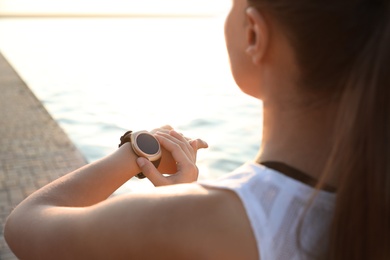 Photo of Woman checking fitness tracker after training near river, closeup