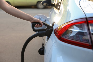 Photo of Woman inserting plug into electric car socket at charging station, closeup