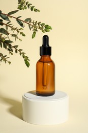 Photo of Bottle with cosmetic oil on podium and green branch on beige background
