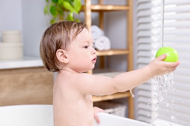 Cute little child playing with ball in bathtub at home