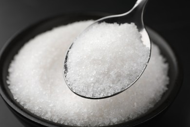 Photo of Spoon with granulated sugar over bowl, closeup