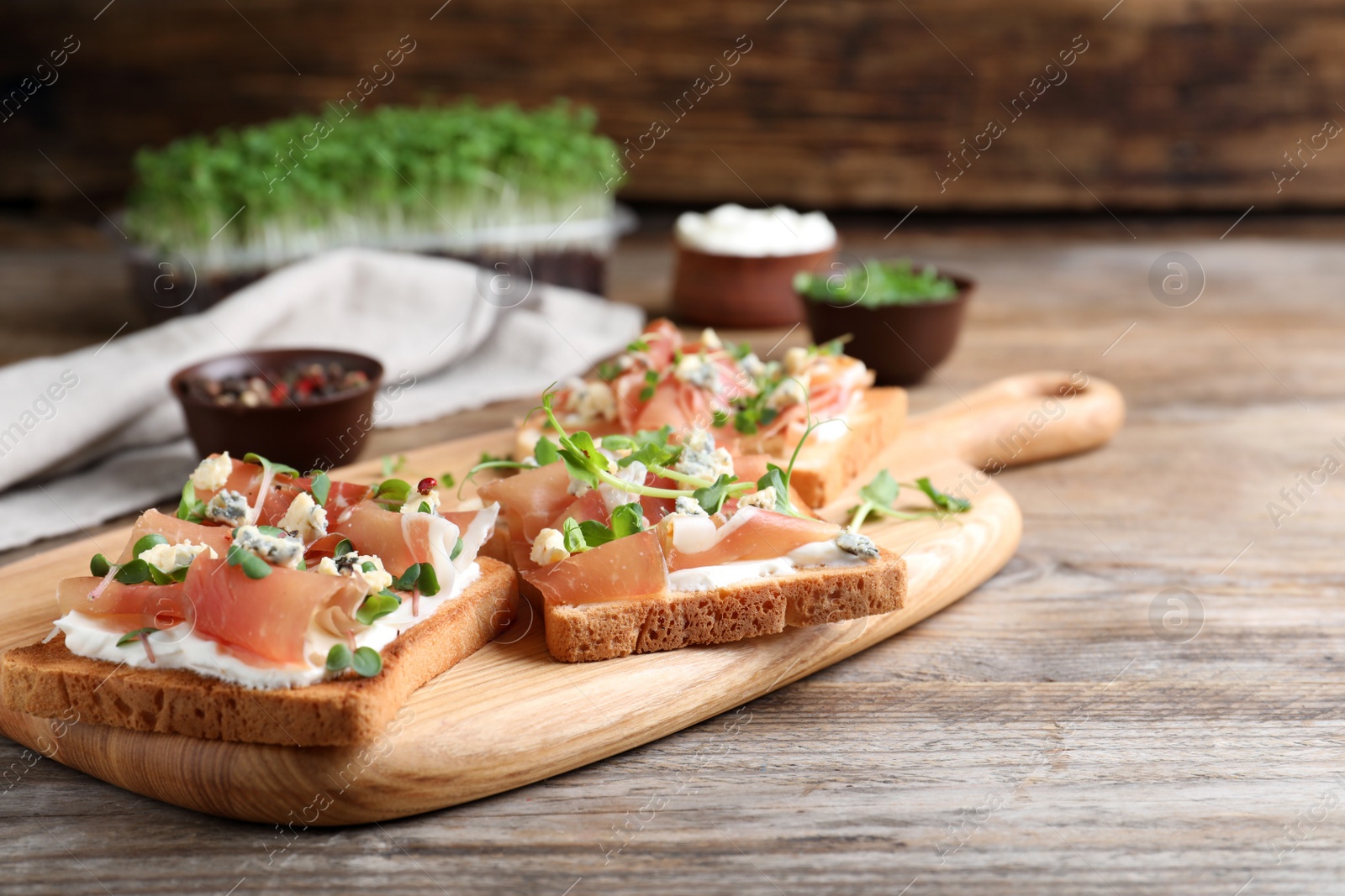 Photo of Delicious sandwiches with prosciutto, cheese and microgreens on wooden table. Space for text