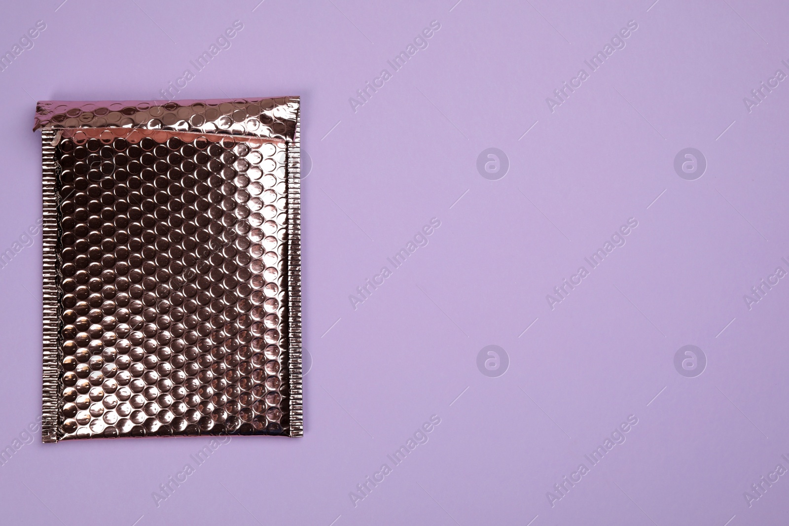 Photo of Padded envelope with bubble wrap on lilac background, top view. Space for text