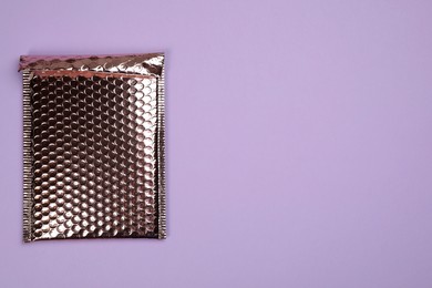 Photo of Padded envelope with bubble wrap on lilac background, top view. Space for text