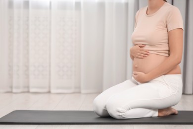 Photo of Pregnant woman sitting on yoga mat at home, closeup. Space for text