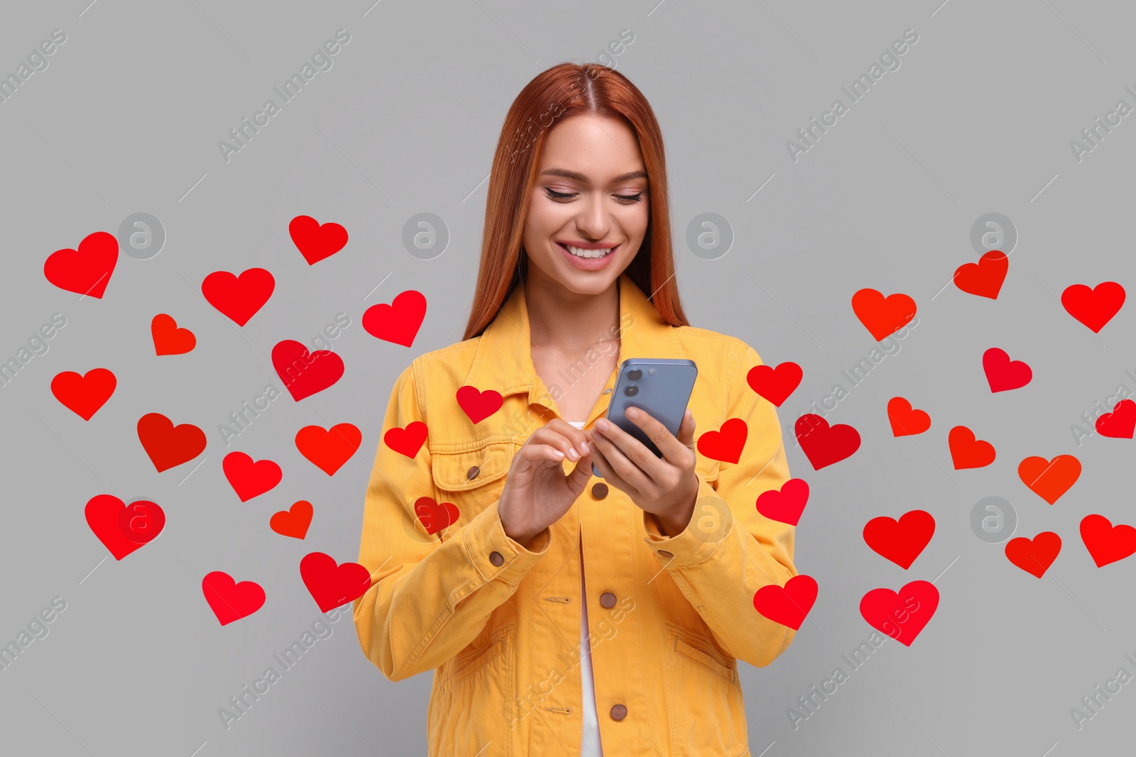 Image of Long distance love. Woman chatting with sweetheart via smartphone on grey background. Hearts flying out of device and swirling around her