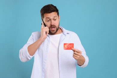 Emotional man with credit card talking on smartphone against light blue background. Be careful - fraud