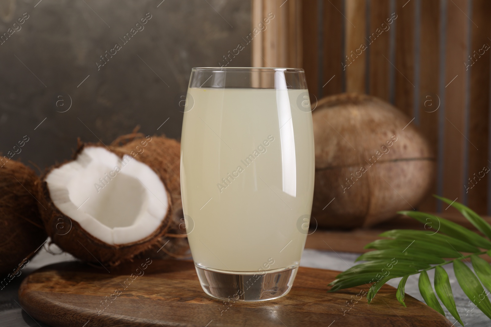 Photo of Glass of coconut water, palm leaf and nuts on grey table