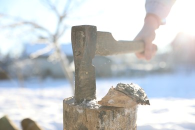 Man taking axe out of wooden log outdoors on sunny day, closeup