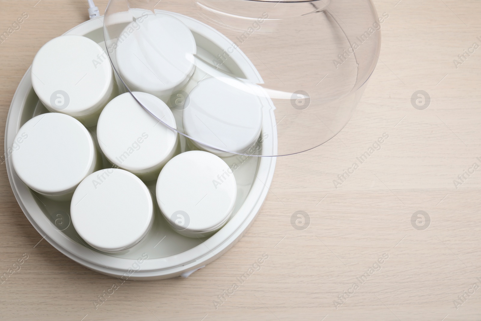Photo of Modern yogurt maker with jars on white wooden table, top view. Space for text
