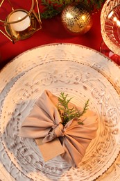 Photo of Furoshiki technique. Gift packed in beige fabric, blank card and festive decor on red table, flat lay