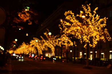 Photo of Blurred view of street with beautiful lights on trees and cars at night. Bokeh effect
