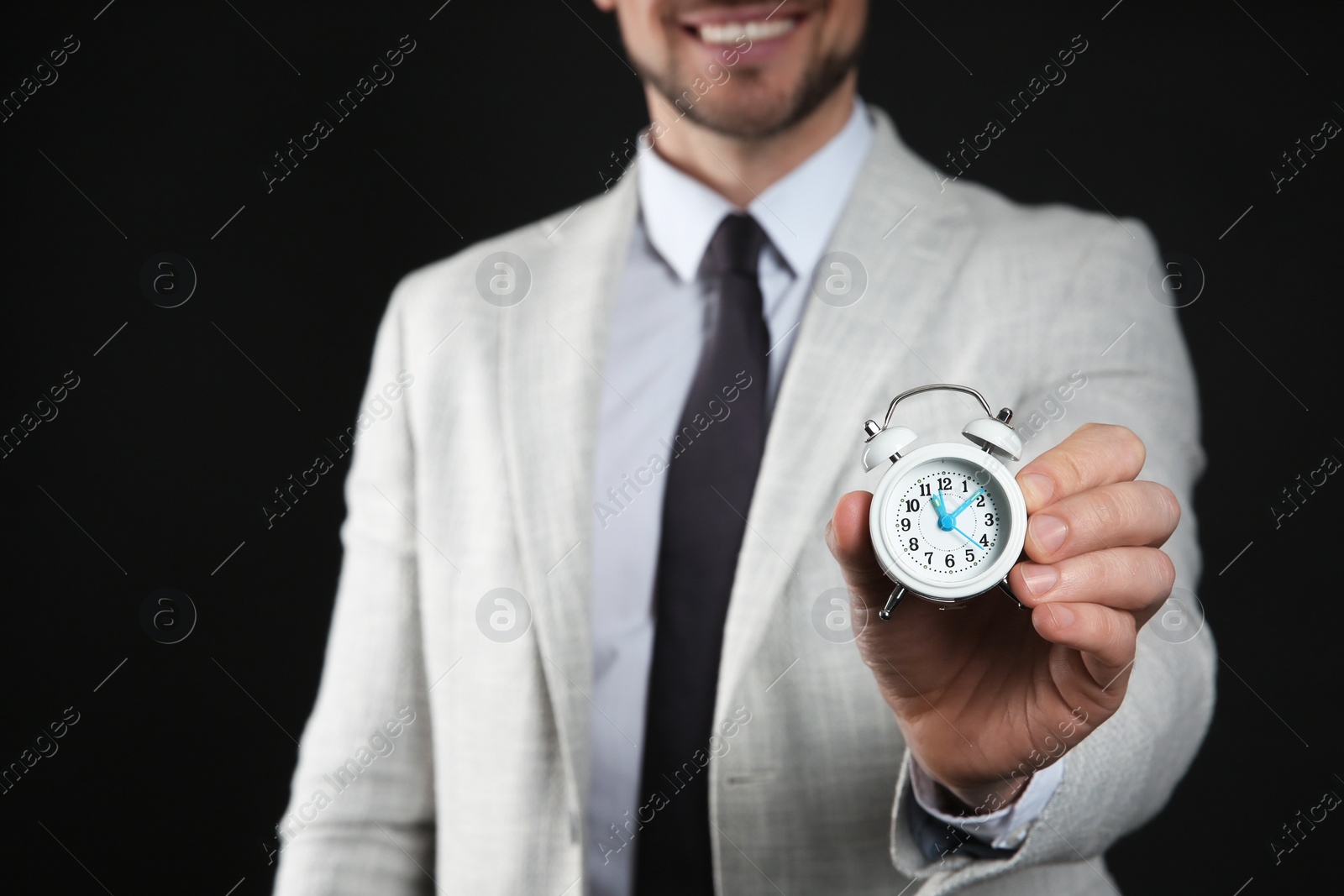 Photo of Happy businessman holding tiny alarm clock on black background, closeup. Time management