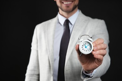 Photo of Happy businessman holding tiny alarm clock on black background, closeup. Time management
