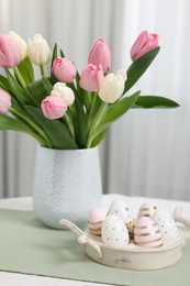 Photo of Easter decorations. Bouquet of tulips and painted eggs on white table indoors, closeup