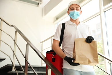 Courier in protective mask and gloves with order indoors. Restaurant delivery service during coronavirus quarantine