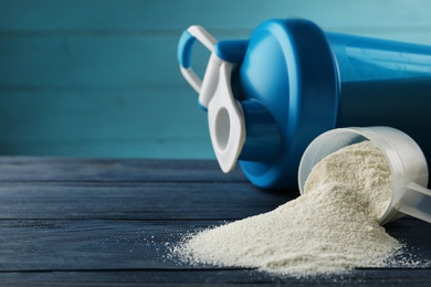 Measuring scoop of protein powder and shaker on blue wooden table, closeup. Space for text