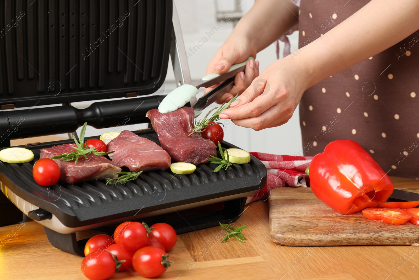 Photo of Woman cooking different products with electric grill at wooden table in kitchen, closeup