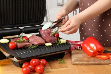 Photo of Woman cooking different products with electric grill at wooden table in kitchen, closeup