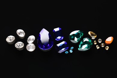 Different beautiful gemstones for jewelry on black background, flat lay