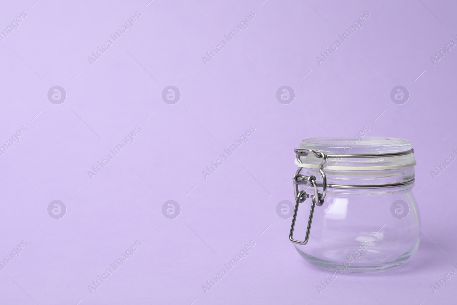 Photo of Closed empty glass jar on lilac background, space for text