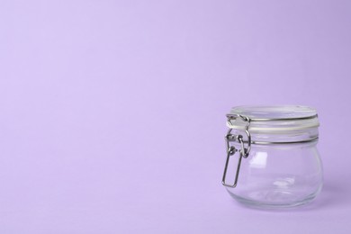 Closed empty glass jar on lilac background, space for text