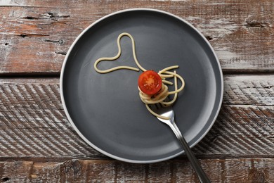 Photo of Heart made of tasty spaghetti, fork and tomato on wooden table, top view