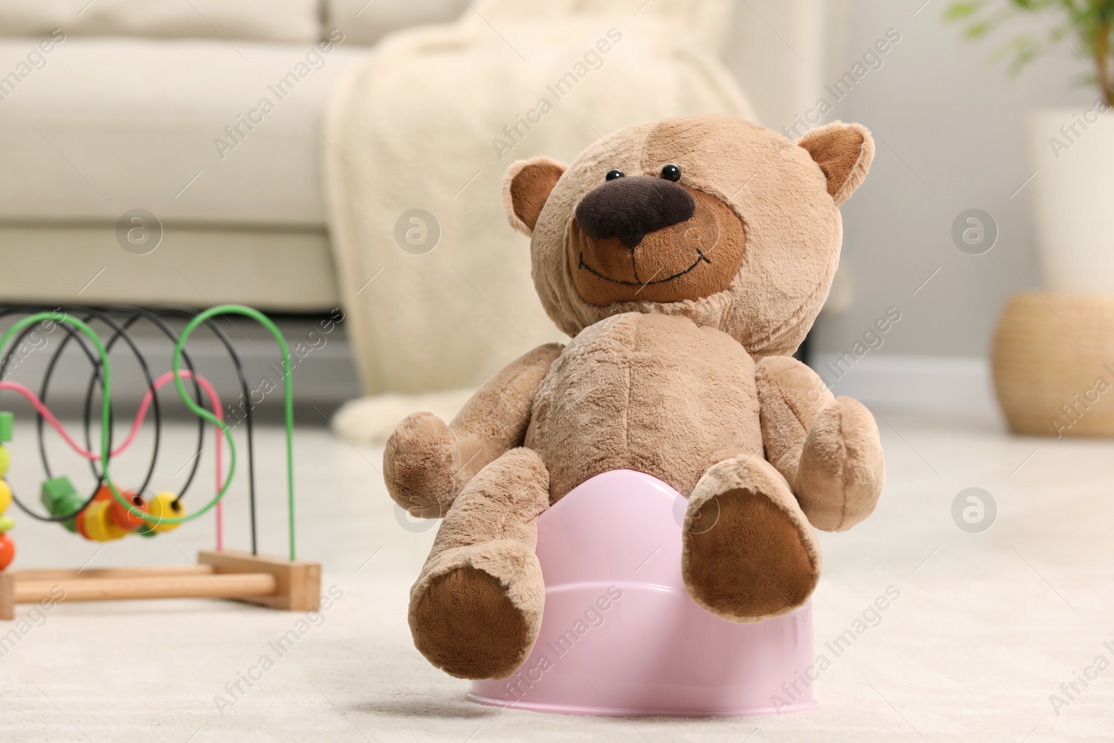 Photo of Cute teddy bear on pink baby potty in room. Toilet training