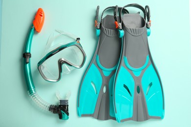 Photo of Pair of flippers, snorkel and diving mask on turquoise background, flat lay