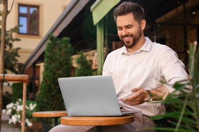 Photo of Handsome young man working on laptop at table in outdoor cafe