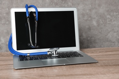 Photo of Laptop with blank screen and stethoscope on table against grey background, space for text. Computer repair