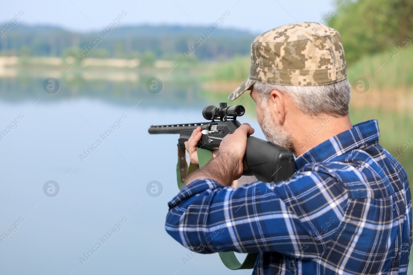 Photo of Man aiming with hunting rifle near lake outdoors. Space for text