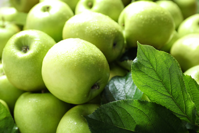 Photo of Pile of wet green apples with leaves as background, closeup