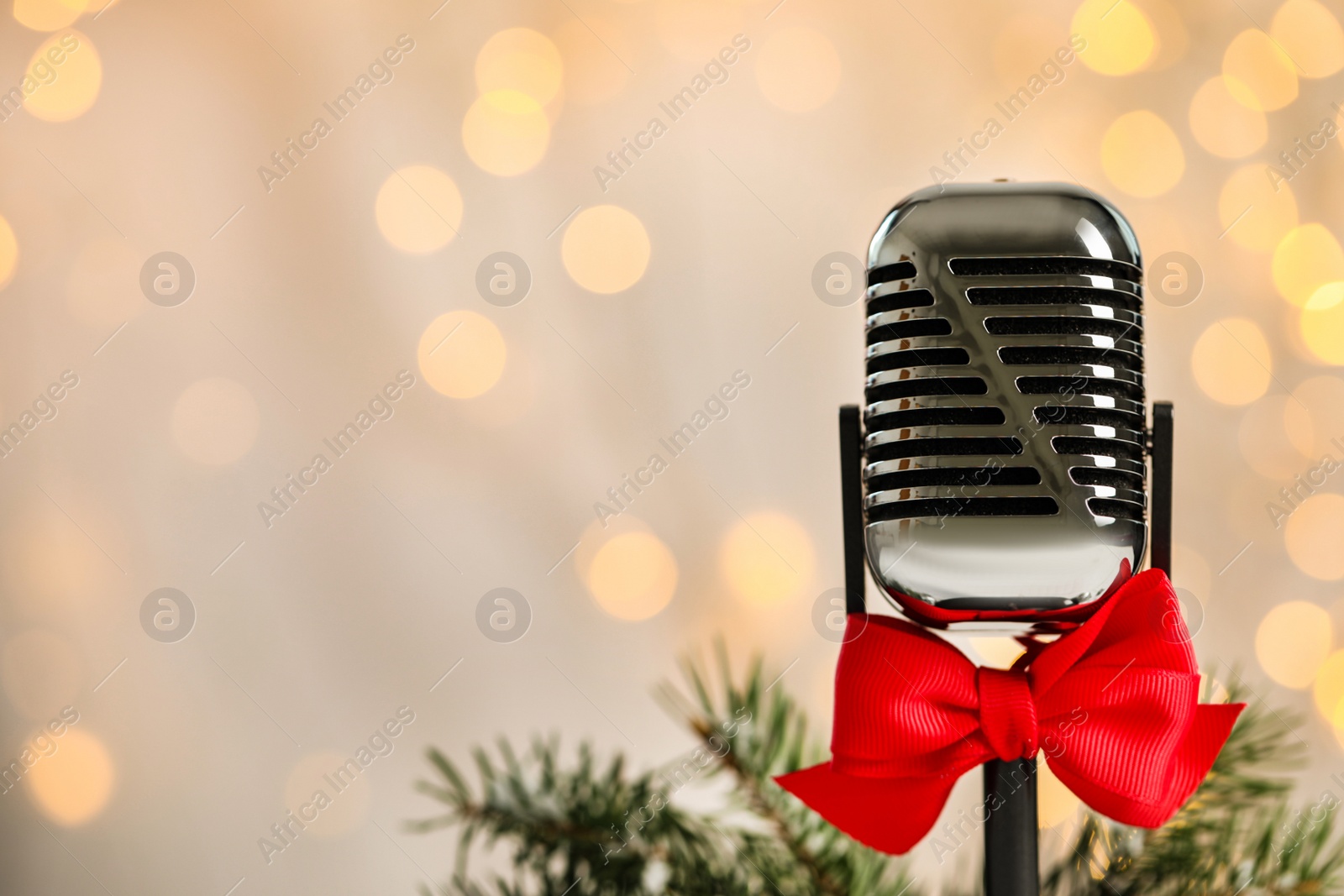 Photo of Microphone with red bow and fir branches against blurred lights, space for text. Christmas music