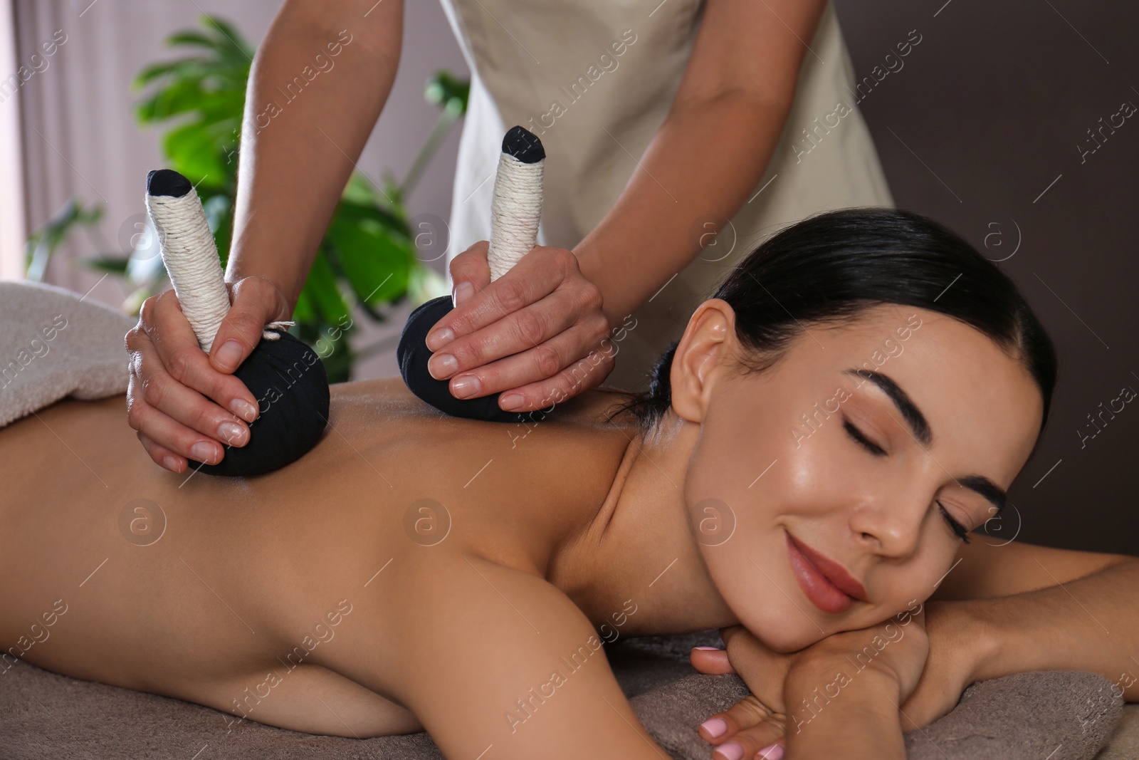 Photo of Young woman receiving herbal bag massage in spa salon