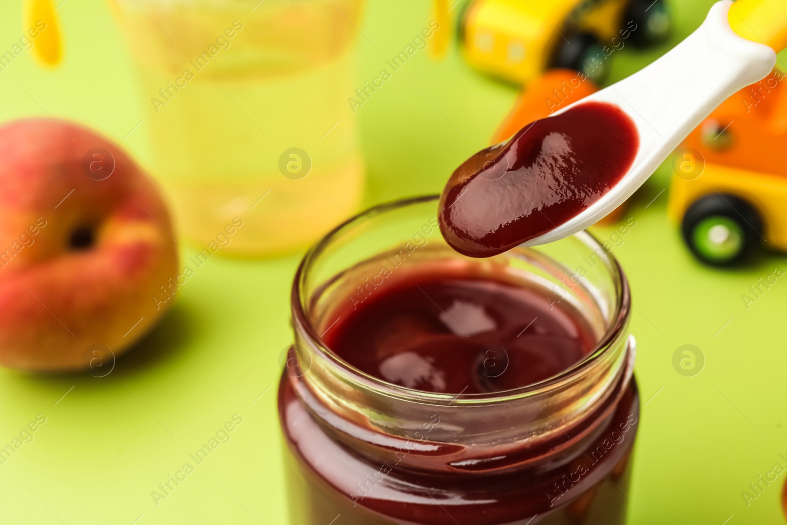 Photo of Spoon with healthy baby food over glass jar on light green background, closeup