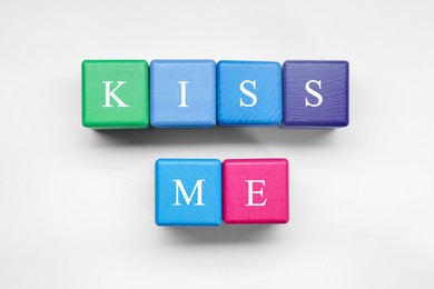 Photo of Colorful cubes with phrase Kiss Me on white background, flat lay