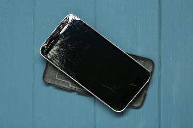 Photo of Damaged smartphone on light blue wooden table, top view. Device repairing