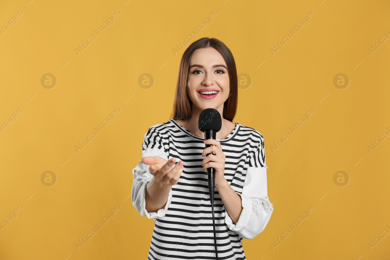 Photo of Young female journalist with microphone on yellow background