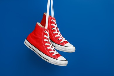Photo of Pair of new stylish red sneakers hanging on laces against blue background