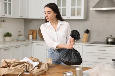Photo of Garbage sorting. Woman with plastic bag at table in kitchen