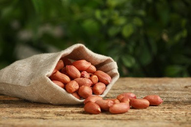 Fresh unpeeled peanuts in sack on wooden table against blurred background