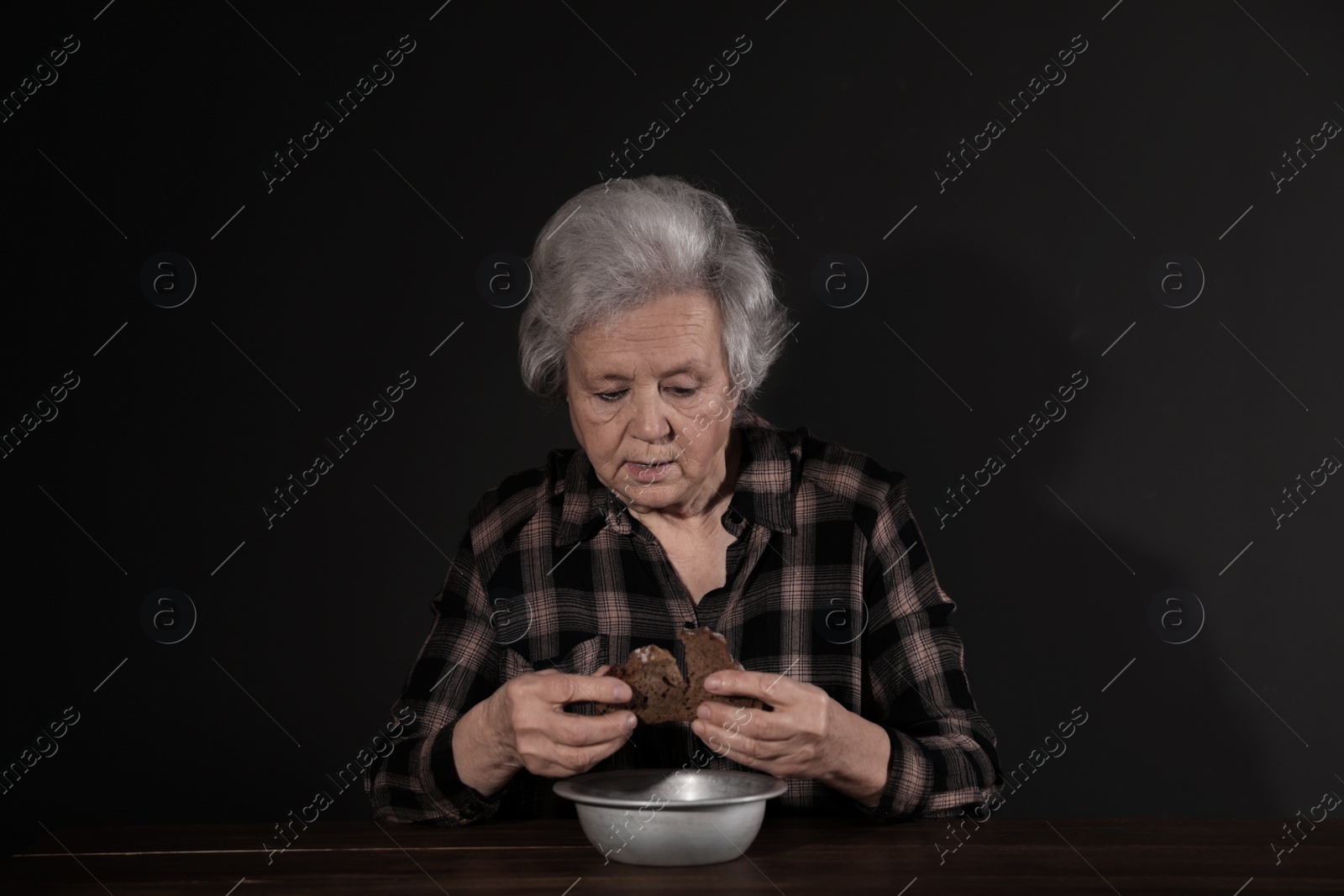 Photo of Poor mature woman with bread and bowl at table